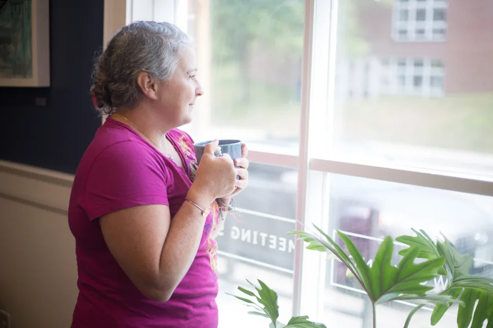 A woman holding a mug and looking out of a window in the morning